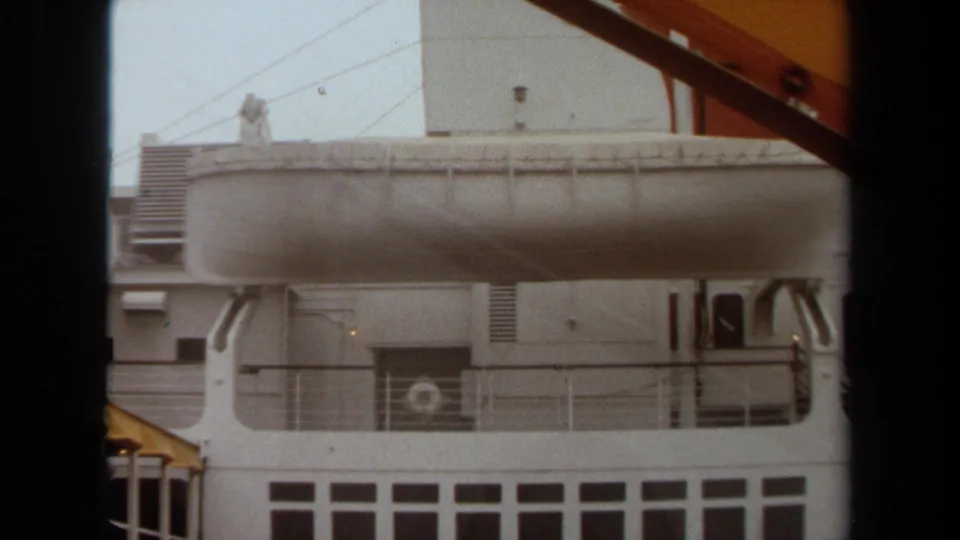 1971 Long Beach frame showing the ship's lifeboat, railings, vents, rectangular windows, portholes, and a yellow gangway corner.