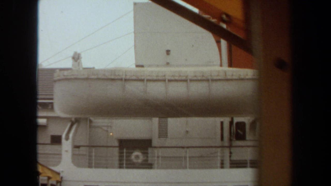 1971 Long Beach home-movie view of a white ship side with lifeboat and railings, partly framed by dark interior edges.