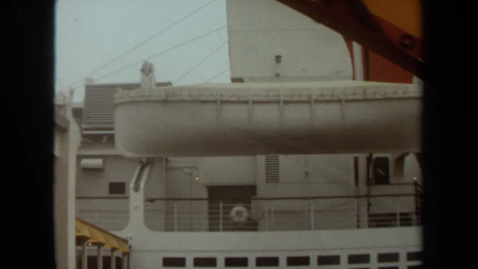 1971 Long Beach view of a cruise or passenger ship's white deck structures, lifeboat, vents, and railings through a dark frame.