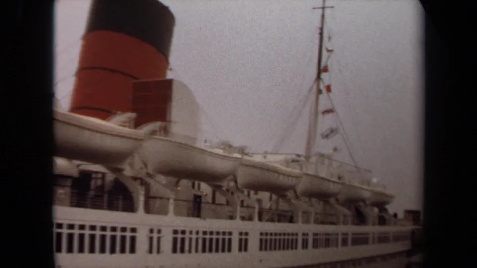 1971 Long Beach frame of a passenger ship side, showing lifeboats, railings, rows of windows, a mast with flags, and the red-and-black funnel.