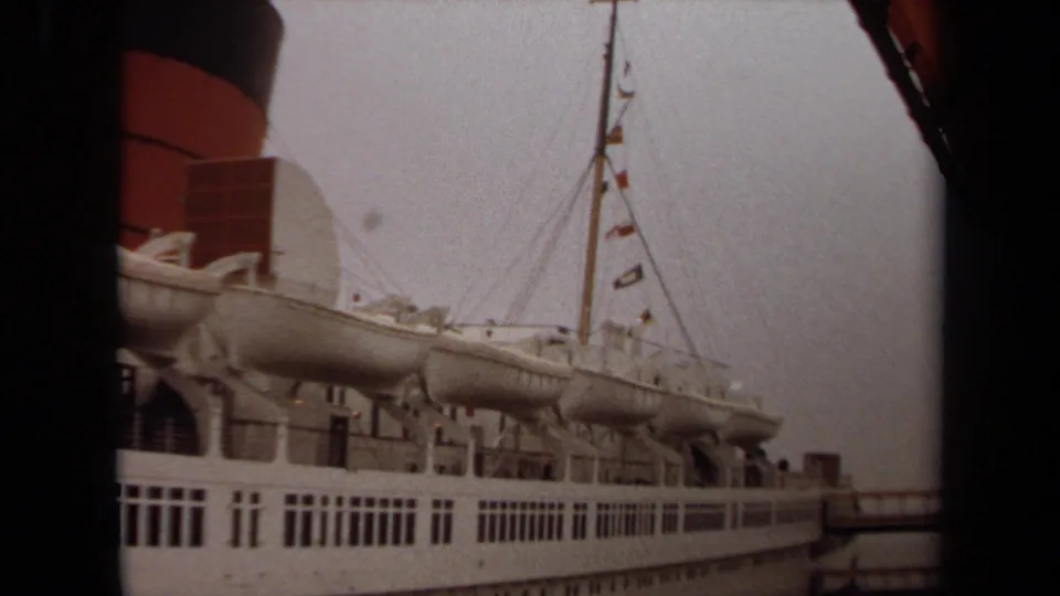 1971 Long Beach frame showing the ship's upper decks, lifeboats, mast rigging with small flags, and red-and-black smokestack.