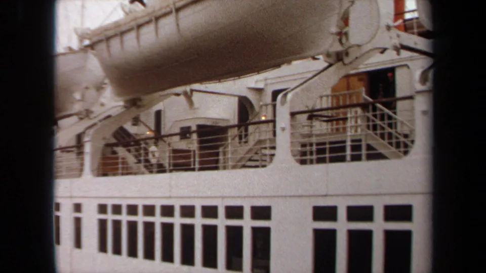Close 1971 Long Beach view of the ocean liner's side, with a lifeboat above deck railings, stairs, doors, and rectangular windows.