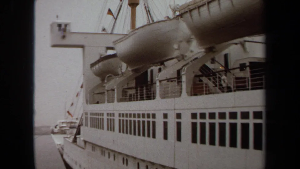 1971 Long Beach home-movie view of a docked passenger ship, with lifeboats overhead, deck railings, window rows, and harbor water glimpsed nearby.