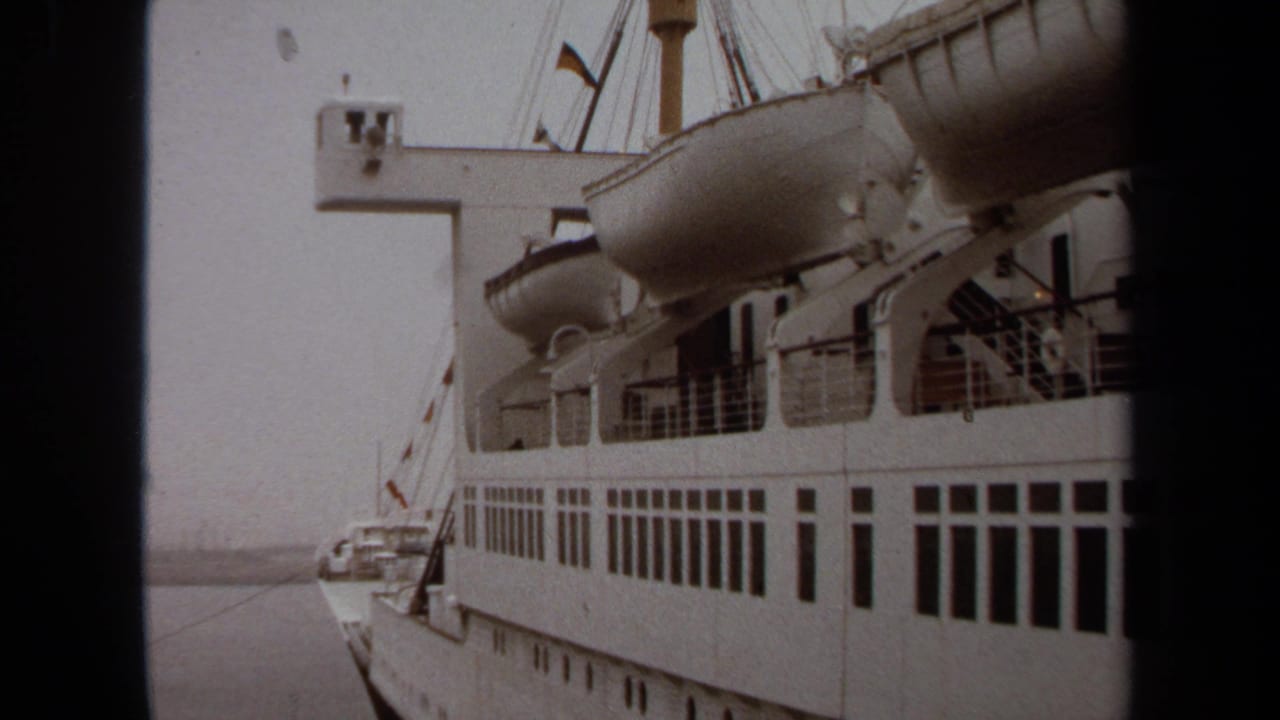 White passenger ship exterior with lifeboats, railings, and hazy water beside the hull.