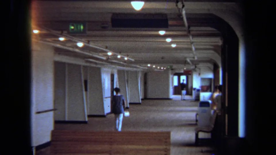 A woman in blue and white walks along a carpeted vessel corridor in 1971 Long Beach home-movie footage.