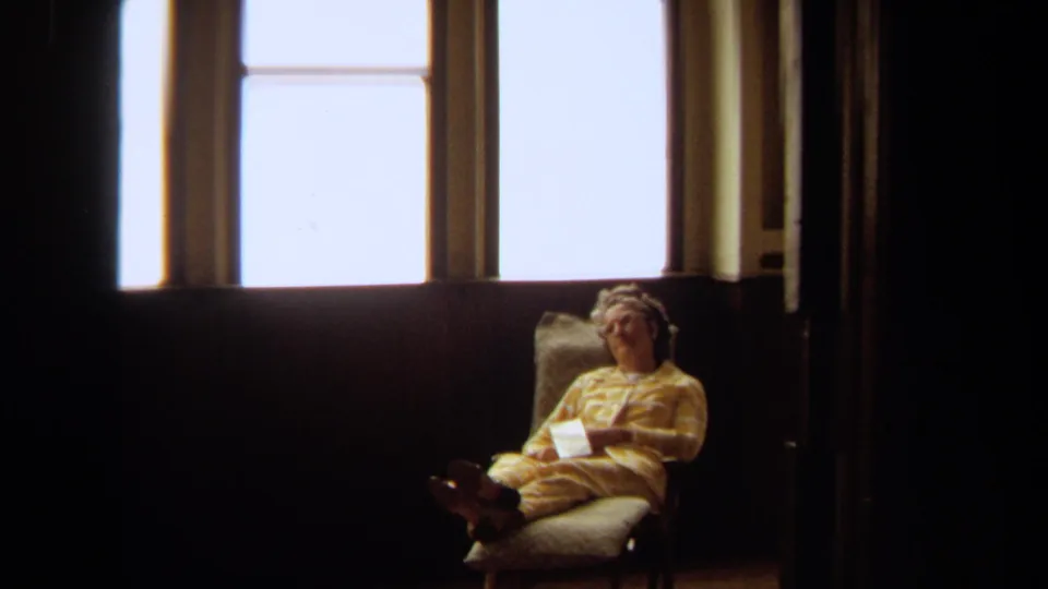 Closer 1971 Long Beach frame of an elderly woman appearing to doze in a lounge chair beneath a bright window.