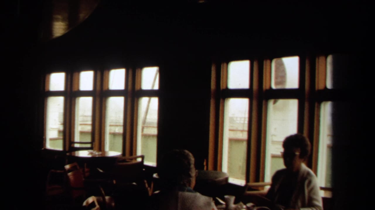 Dim ship interior with seated passengers silhouetted near large windows.
