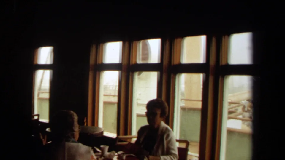 1971 Long Beach ship interior view with silhouetted passengers at tables and daylight through wood-framed windows onto exterior deck details.