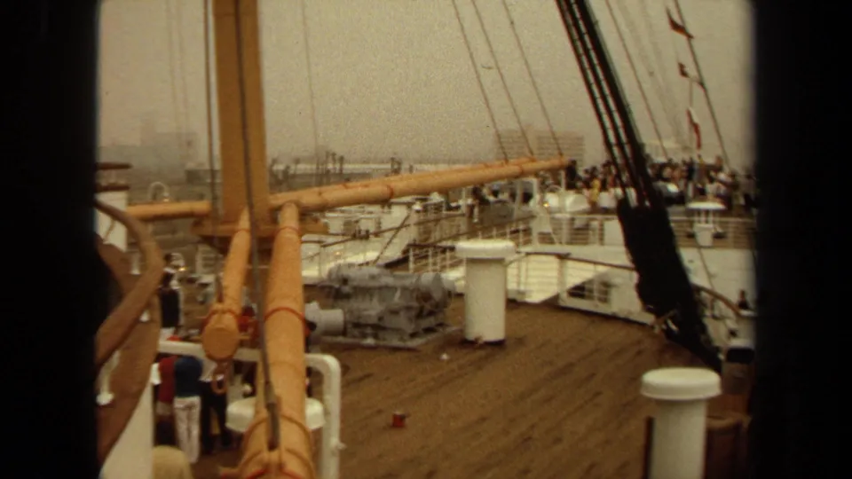 Wide 8mm deck view from a Cunard ship sequence, showing passengers near railings with rigging and harbor structures in the background.
