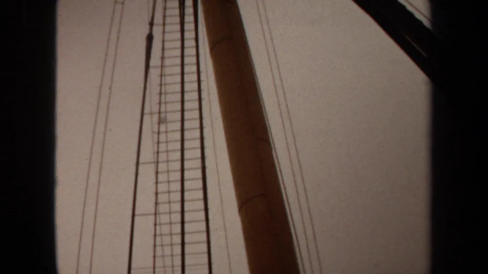 1971 Long Beach 8mm frame with vertical ladder rigging, wooden mast, thin wires, pale sky, and a dark diagonal boat edge.