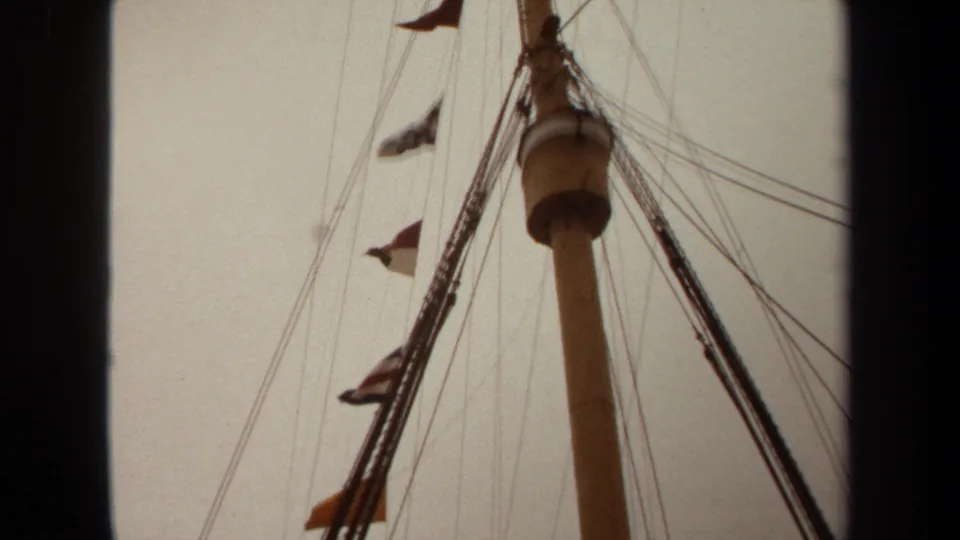 1971 Long Beach 8mm frame with a tall ship mast, rigging lines, and small flags fluttering near the upper mast.
