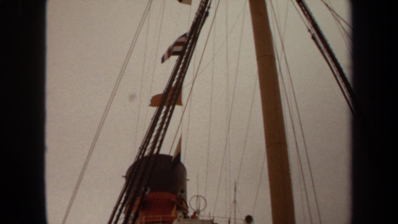 Ship funnel, mast, rigging, and upper bridge seen from below against an overcast sky.