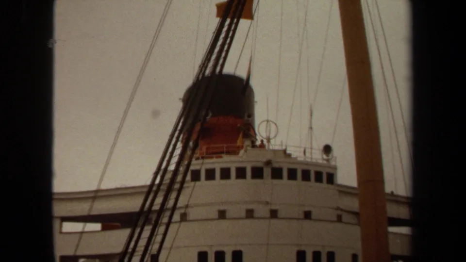 1971 Long Beach 8mm frame with a low-angle view of ship bridge windows, funnel, mast, rigging, and a pale sky.