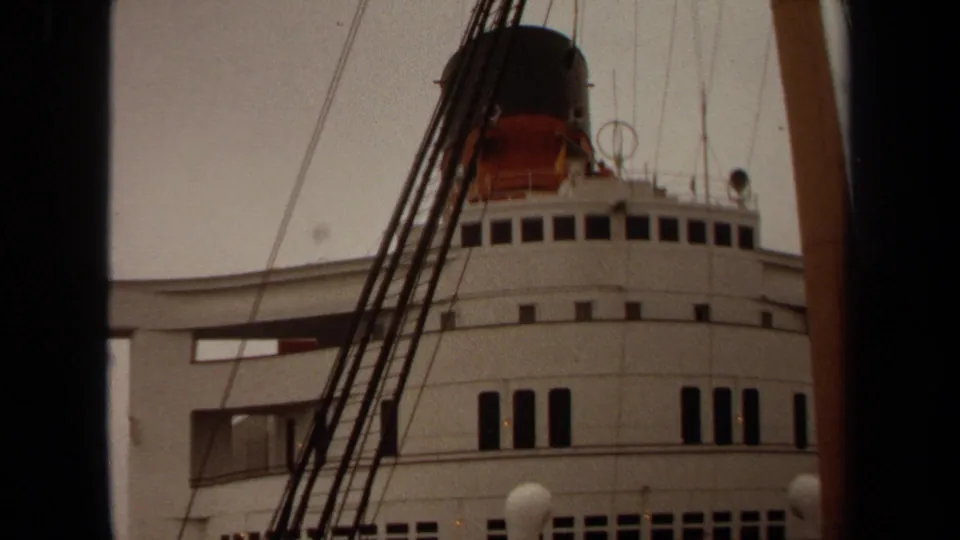 1971 Long Beach home-movie frame of a white passenger ship exterior with rows of windows, rigging, and a dark funnel above.