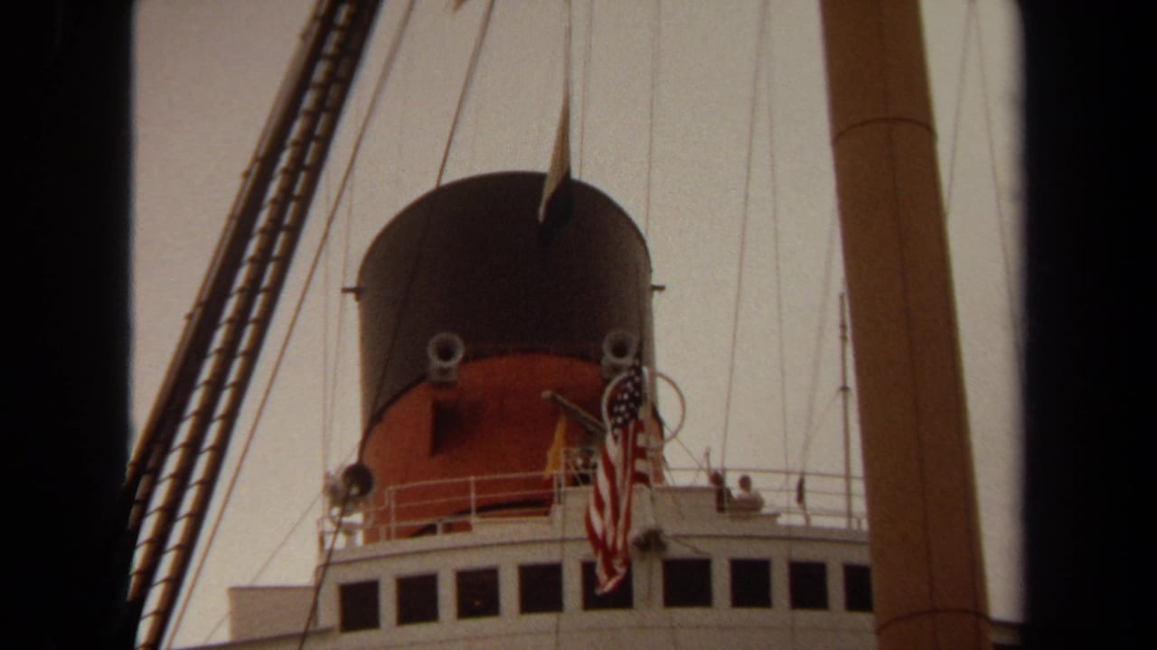 1971 Long Beach home-movie frame looking up at a ship funnel, U.S. flag, rigging, bridge windows, and railings.