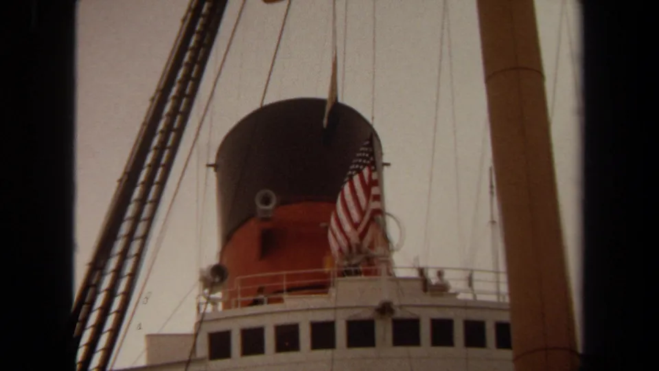 1971 Long Beach frame of an ocean liner funnel with an American flag, rigging, and white superstructure below.