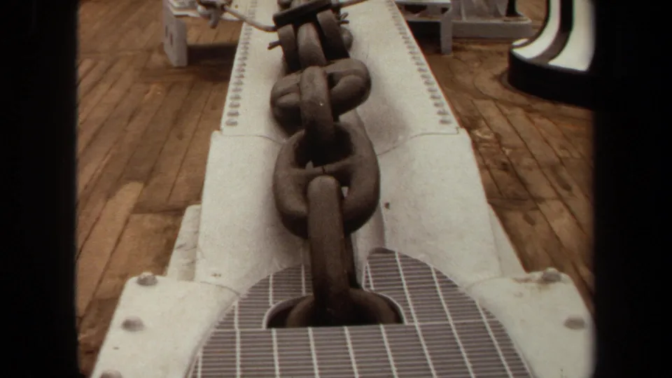 Large anchor chain seen from above on white shipboard machinery, with wooden deck planks nearby.