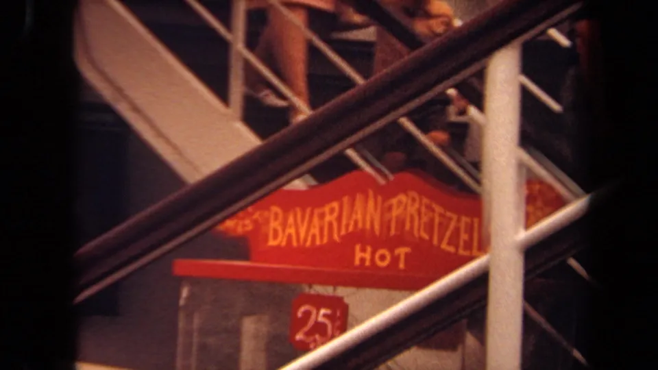 Long Beach ship-deck frame with people on stairs above a red hot Bavarian pretzels sign and railings.