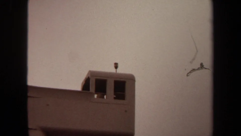 1971 Long Beach frame with the upper portion of a pale lookout-like structure, two dark windows, a roof antenna, and hazy sky.