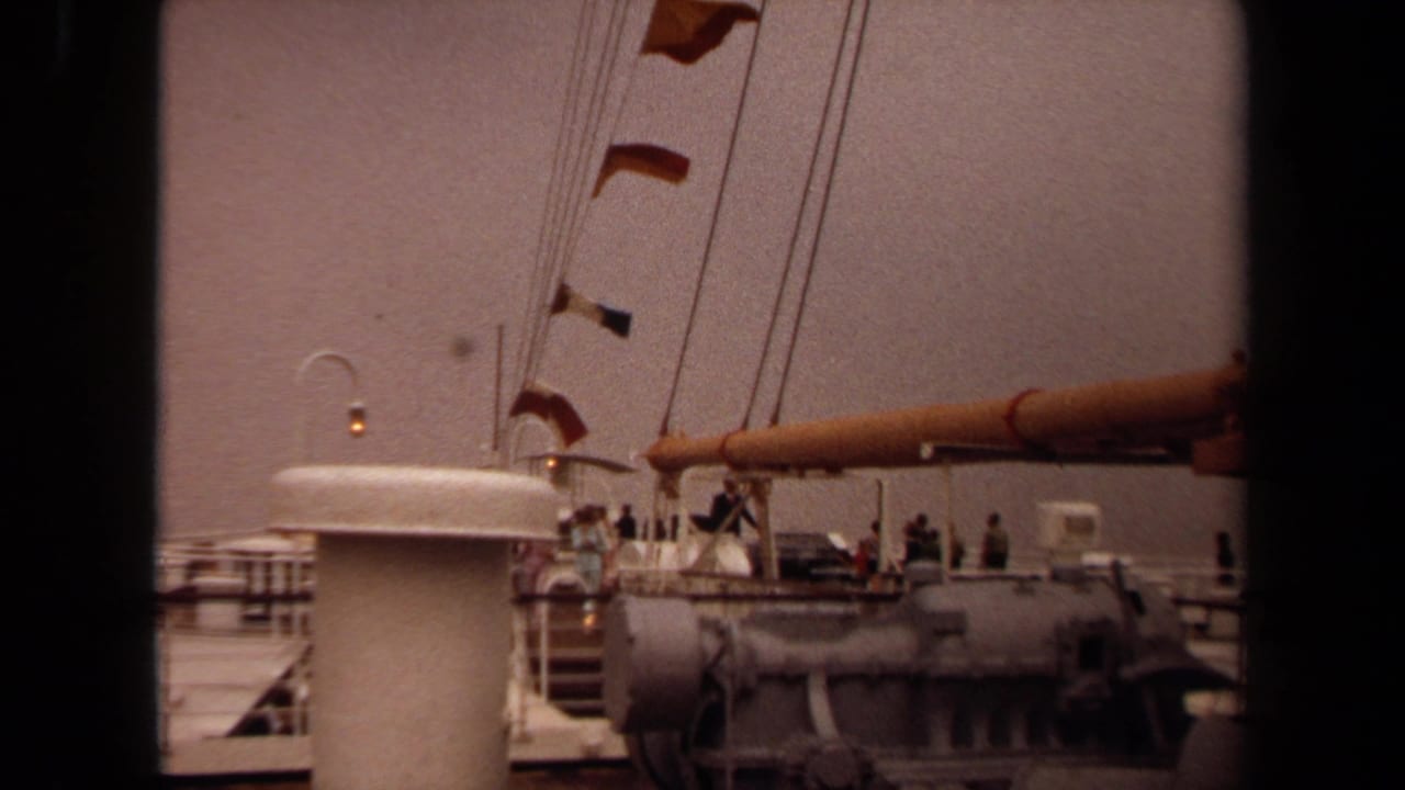 1971 8mm Long Beach shipboard view with a white funnel, signal flags, rigging, and passengers along the deck railing.
