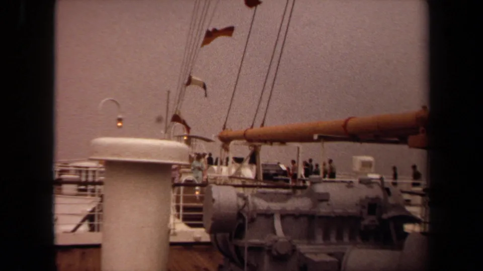 1971 Long Beach 8mm frame showing passengers on a ship deck below rigging and fluttering signal flags.