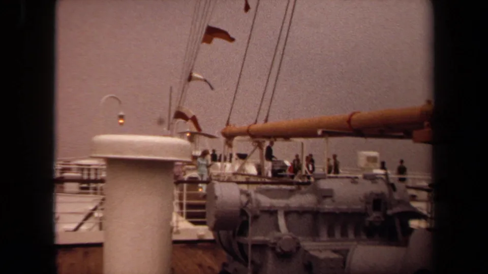 Warm 8mm Long Beach ship deck view from 1971, with flags, rigging, passengers, railings, and a white funnel visible.