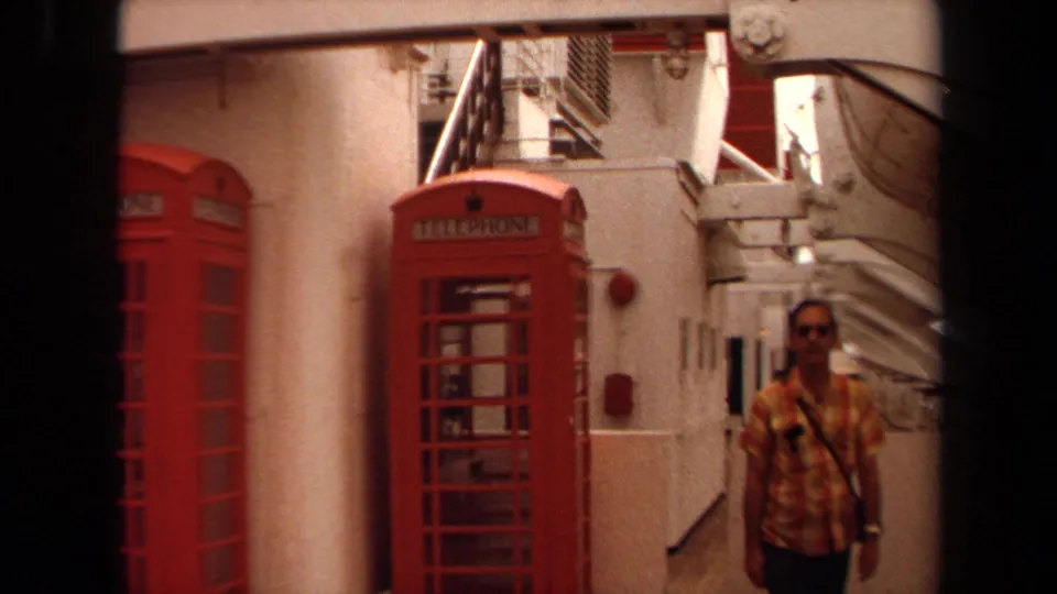 1971 Long Beach home-movie frame showing a man walking on a cruise ship deck beside red telephone booths.