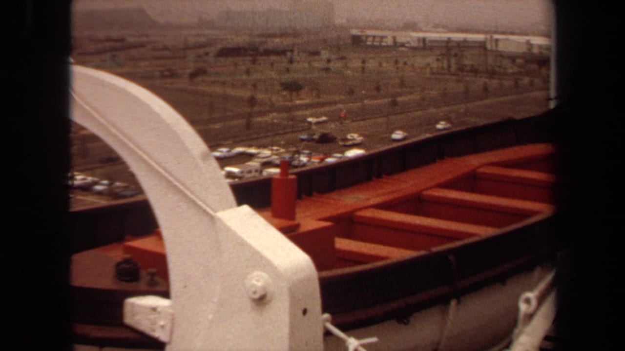 White ship davit and red lifeboat seen from a deck above parked cars and a roadway.