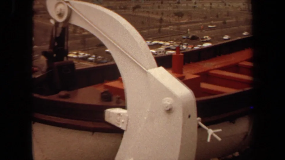 1971 Long Beach deck angle showing a curved white davit, red lifeboat, deck fittings, roadway, and rows of cars below.