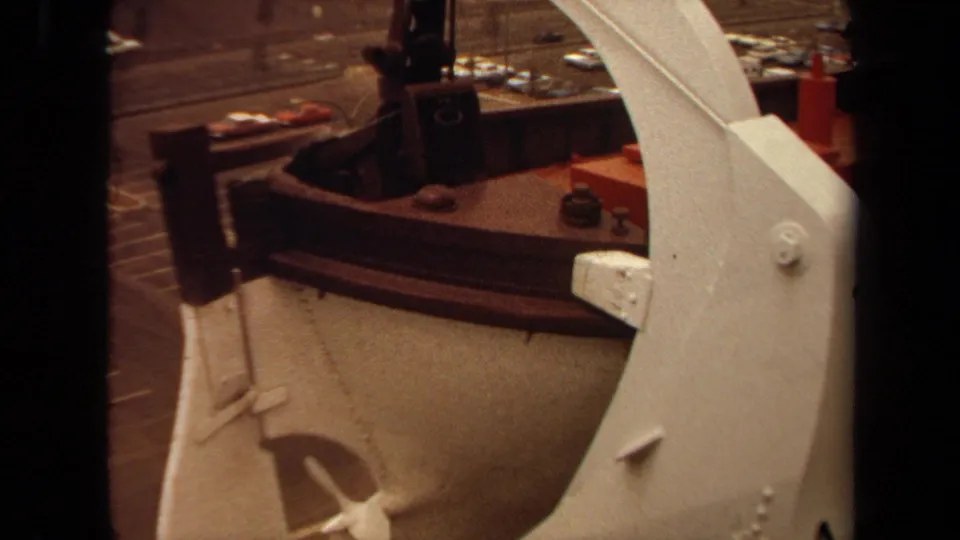 1971 Long Beach deck view with white davit hardware above a lifeboat, plus ship railing, dockside road, and cars beyond.