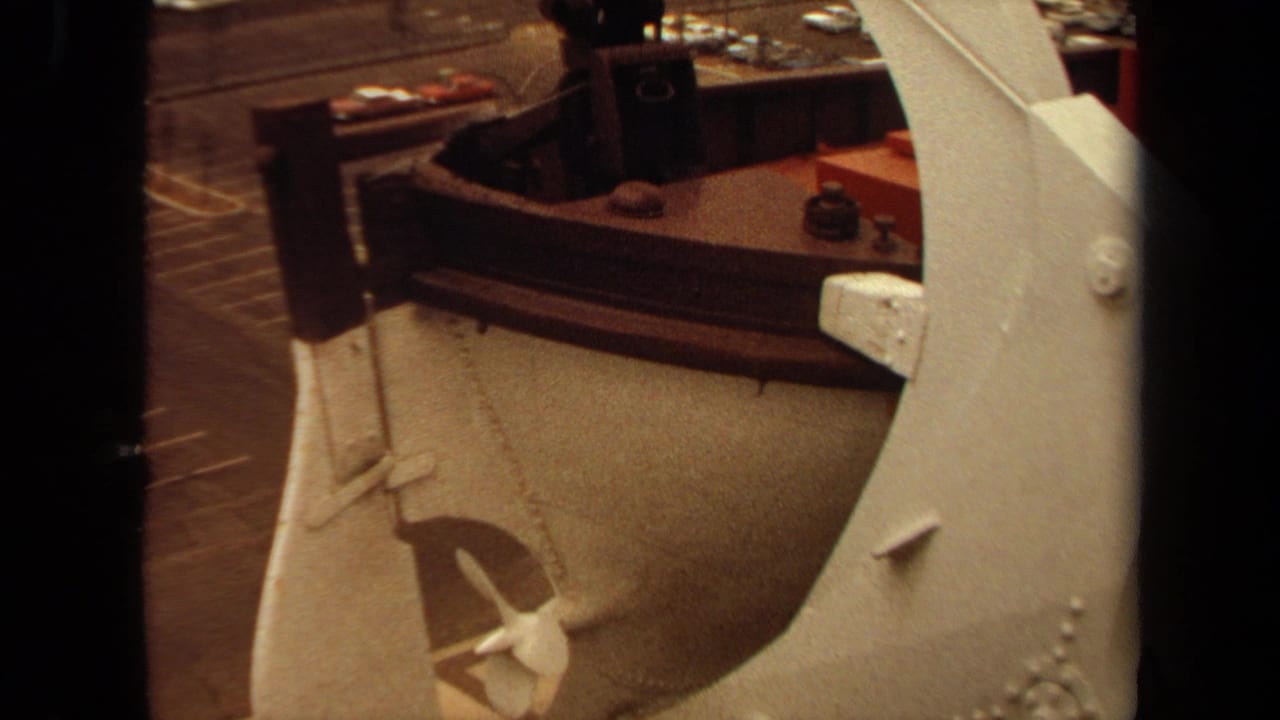 Close view of a brass-colored industrial machine beside a work area, partly obscured by dark film edges.