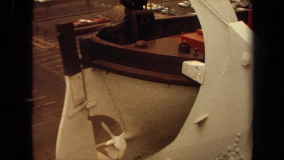 1971 Long Beach 8mm frame showing a brass-toned industrial machine and nearby work surface inside a factory or workshop.