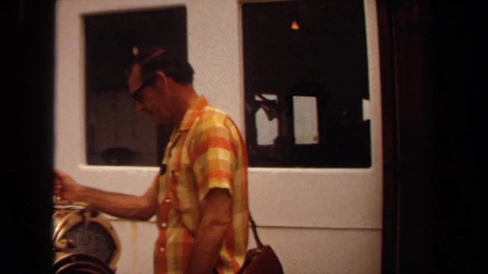 1971 Long Beach frame of the same man beside industrial machinery, seen through a dark vertical film-frame division.