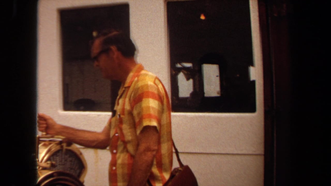 In 1971 Long Beach travel footage, a man in glasses and a striped shirt stands on a boat deck near windows and a brass railing.
