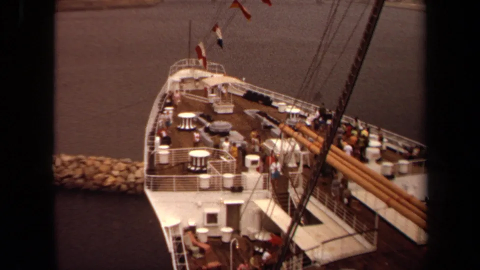The 1971 Long Beach clip ends on a high-angle view of the boat deck with passengers, railings, tables, rigging, flags, and harbor water.