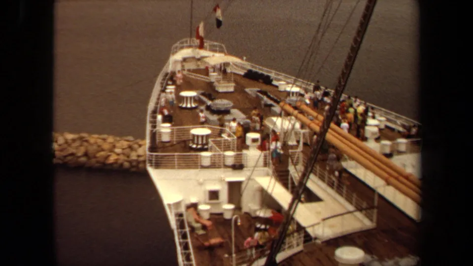 1971 Long Beach home-movie view looking down on a docked passenger ship deck with people, tables, railings, and rigging.