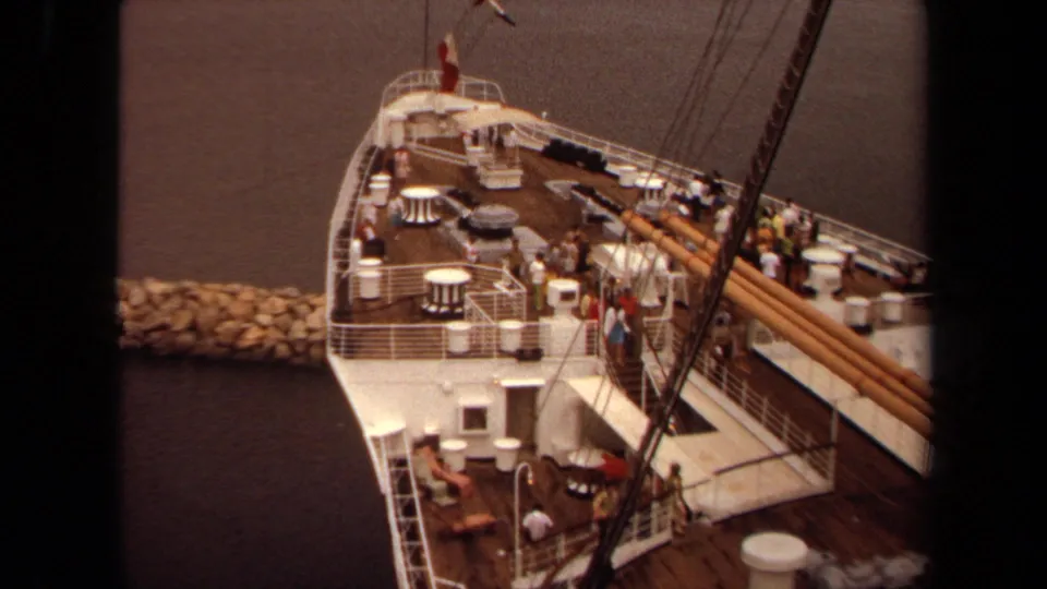 1971 Long Beach cruise ship deck with passengers near white railings, round tables, rigging, and dockside water.