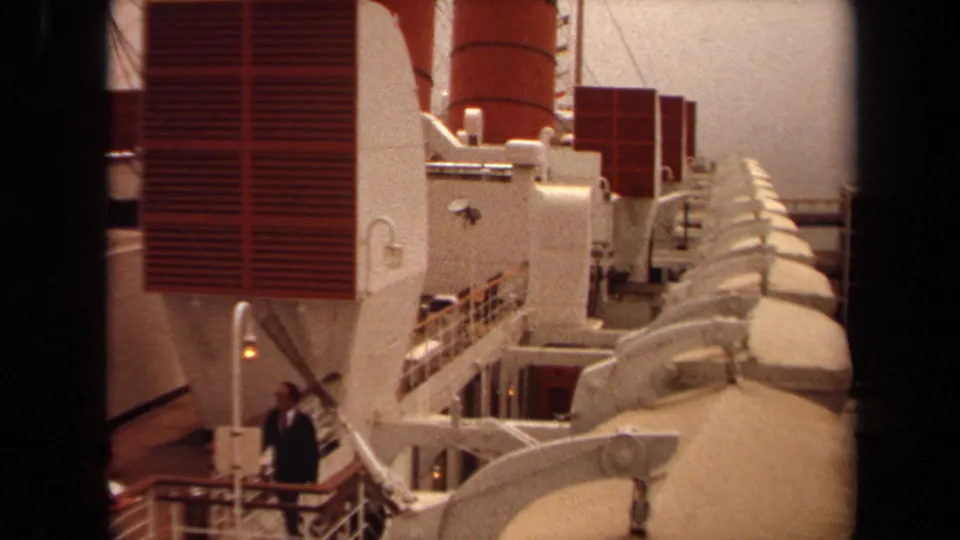 1971 Long Beach frame of an ocean liner deck with red ventilation panels, rows of lifeboats, railings, and a figure near the stairs.
