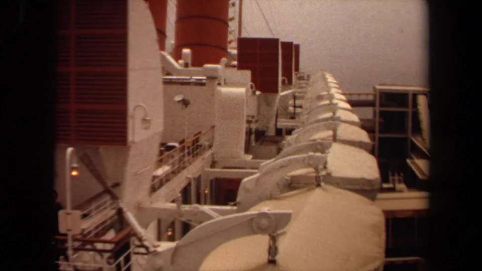 1971 Long Beach home-movie frame looking along a ship deck with lifeboats, railings, stairs, and red and white funnel structures.