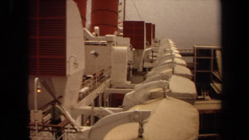 1971 Long Beach frame showing lifeboats along a large ship deck with red panels, white structures, railings, and background windows.