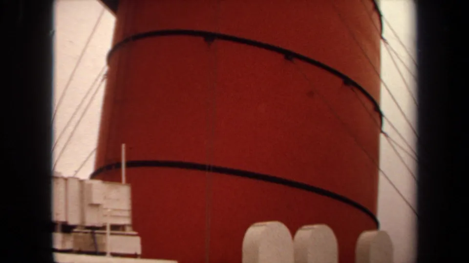 Close 8mm view of the red ship funnel and white deck fixtures, with rigging lines against the sky in Long Beach footage.