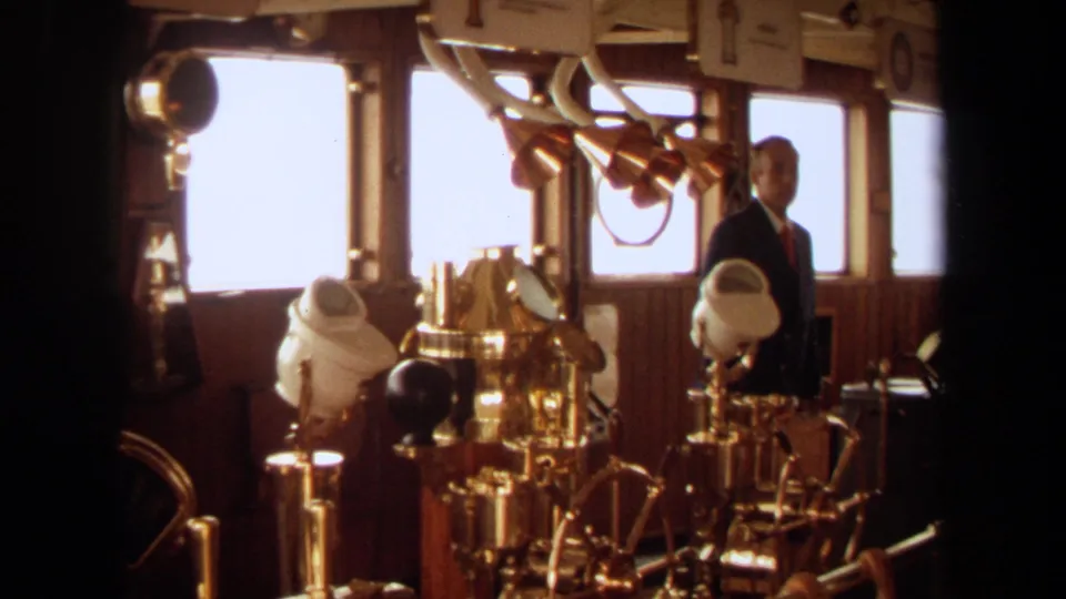 The final frame holds on the vessel bridge, with brass navigation fittings, white instrument housings, and a suited person near the right window.