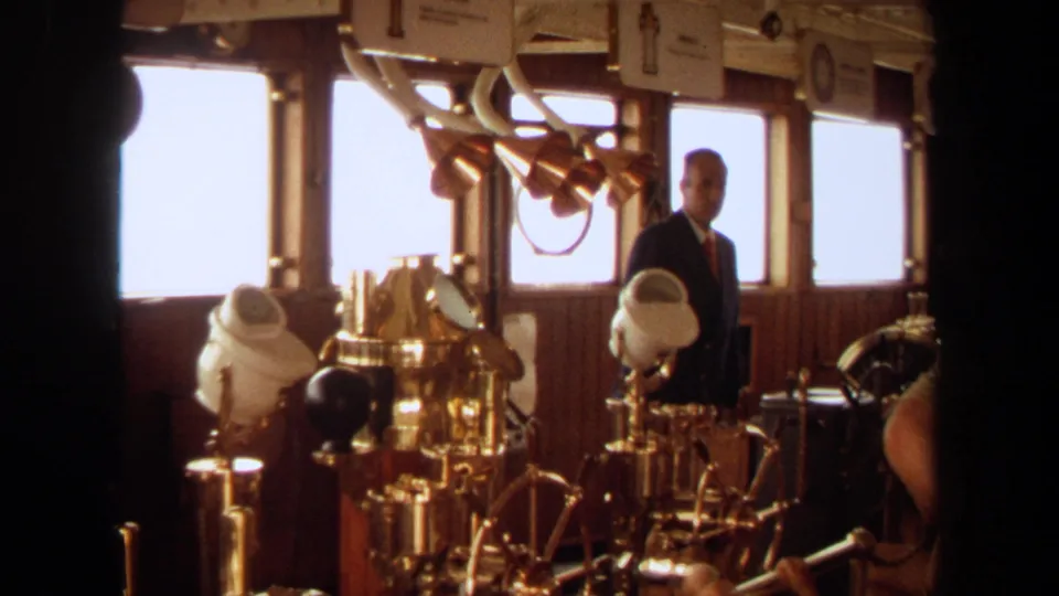 1971 Long Beach yacht bridge interior with a suited man near brass controls, windows, and wood paneling.