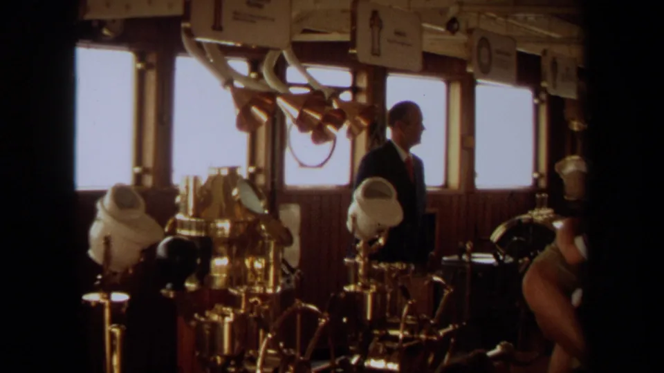 Suited man in profile inside the 1971 Long Beach yacht bridge, with brass instruments and bright windows behind him.