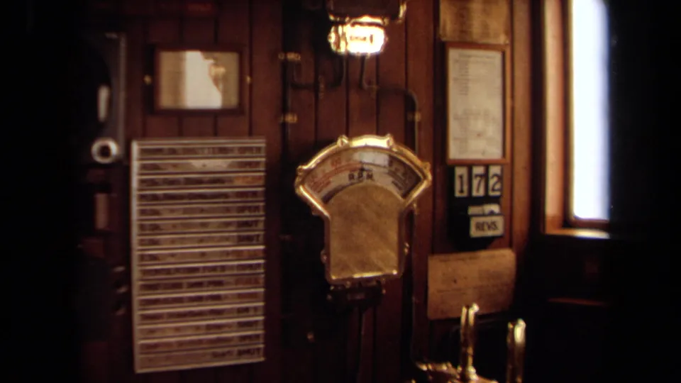 Close view of the yacht bridge interior showing a brass engine telegraph, wall display, wood paneling, and window edge.