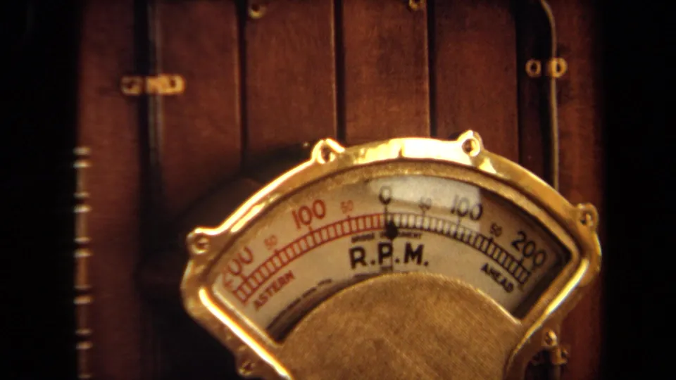 Tight 1971 Long Beach frame of a brass-toned R.P.M. gauge face, showing the dial scale and housing details.