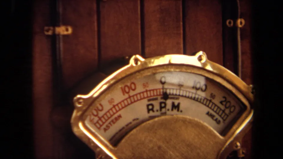 1971 8mm close-up of a brass-toned boat R.P.M. gauge with dark wood paneling behind it.