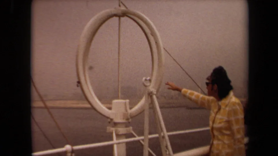 In 1971 Long Beach footage, a man in sunglasses points from a boat deck beside a white circular antenna and railings.