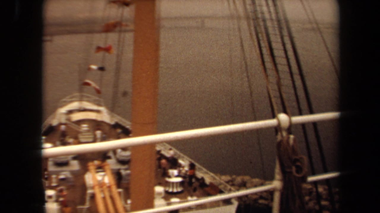 1971 Long Beach passenger ship bow viewed through a window frame, with deck railings, rigging lines, flags, and people visible.