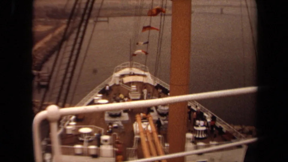 1971 Long Beach view of a large passenger ship deck, with people at the railings, rigging lines, flags, and hazy shoreline beyond.